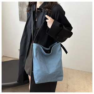 Détail de la texture du sac seau en denim bleu clair et fine bandoulière noire sur modèle