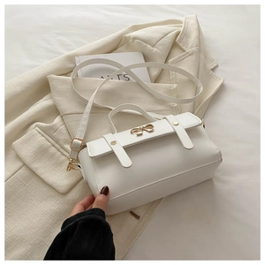 Detail view of white PU leather crossbody bag with a golden metal bow and decorative straps