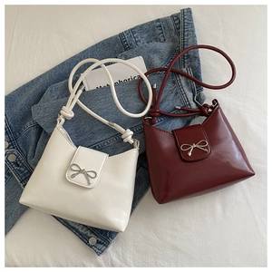 Detail of white and burgundy shoulder bags with silver bow accents on glossy leather