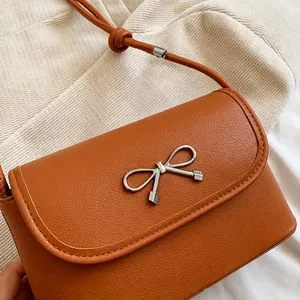 Close-up of brown leather texture and silver metal bow ornament on a chic small handbag