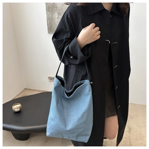 Détail d'un sac hobo en jean bleu avec une fine bandoulière en cuir noir sur un manteau