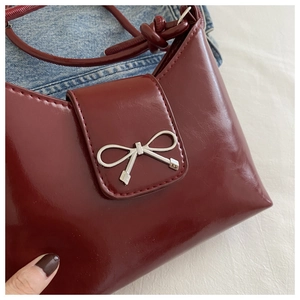 Close-up of wine red glossy PU leather shoulder bag with silver metal bow and knot strap