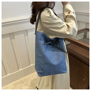 Sac seau chic en denim bleu avec nœud en cuir noir porté par un mannequin en trench-coat