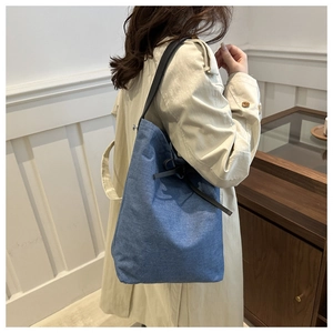 Détail d'un sac seau en jean bleu avec des lanières en cuir noir et un cordon de serrage
