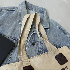 Detail view of canvas tote bag showing dark brown leather trim and printed letters
