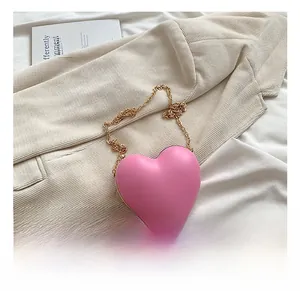 Detailed view of pink heart-shaped crossbody bag with gold chain on a beige fabric