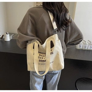 Detail of a beige canvas tote bag with brown leather trim and text in a cafe setting