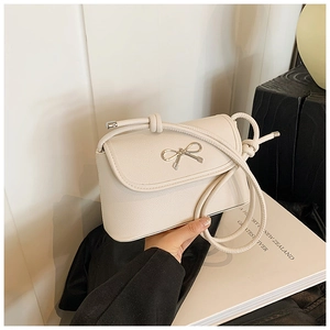 Detail of creamy white litchi grain faux leather bag with silver metal bow and knot strap