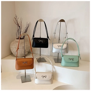 Five small flap bags in vibrant colors with silver bow accents and knotted straps