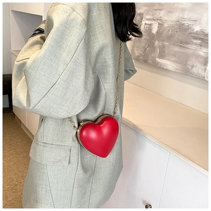 Model wearing a red heart-shaped crossbody bag with a gold chain strap and metal frame clasp