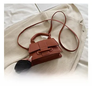 Détail d'un petit sac carré marron à motif litchi posé sur un tissu tissé doux et élégant