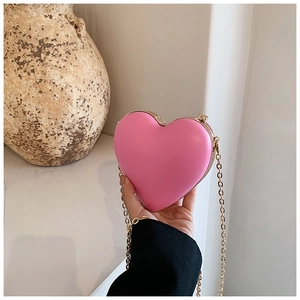 Detail of pink heart-shaped crossbody bag with gold metal trim and chain strap