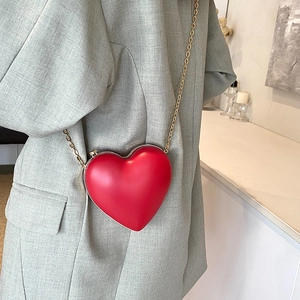 Red heart-shaped crossbody bag with gold chain strap worn by a model in a gray suit