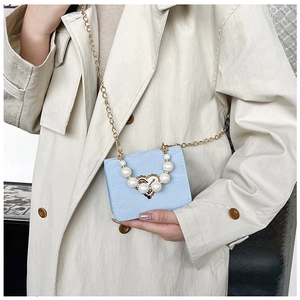Detail view of light blue mini square bag with pearl heart handle and gold chain strap