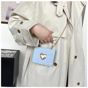 Detail of light blue mini bag with pearl handle, heart buckle, and gold chain strap
