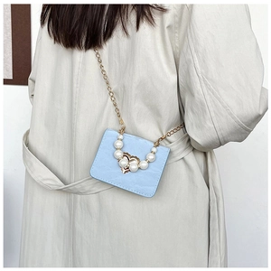 Close-up of light blue mini crossbody bag with pearl chain and golden heart buckle detail