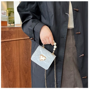 Detail of marble pattern mini bag with pearl handle and golden heart lock on coat background