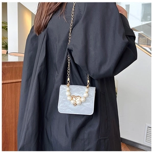 Macro detail of silver pearl handbag with heart-shaped gold lock and chain strap