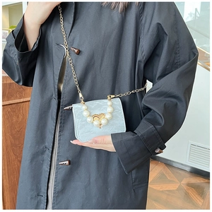 Detail view of mini blue marble crossbody bag featuring a large pearl heart buckle and gold chain