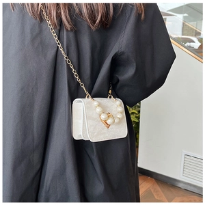 Detail of white mini square bag with large pearl handle and golden heart clasp on model