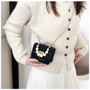Detail of a black pleated mini crossbody bag with pearl handle and gold chain strap