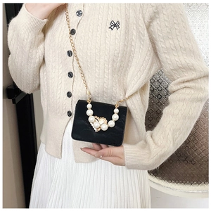 Detail of a mini black leather crossbody bag featuring heart pearl embellishment and chain