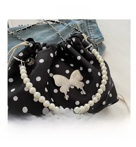 Detail of polka dot satin bucket bag featuring pearl handle and silver butterfly charm