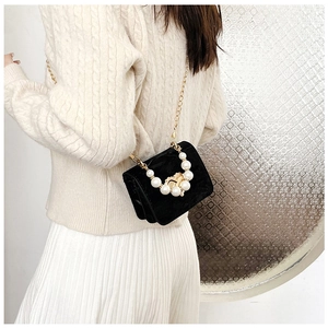 Detail of black velvet mini bag with pearl decor and golden chain strap on a model