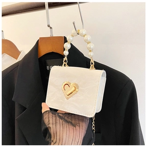 Detail showing elegant white mini bag with pearl handle and golden heart lock on a jacket