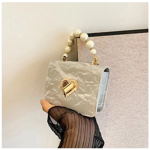Close-up of a mini silver square bag featuring a pearl handle and heart-shaped gold lock