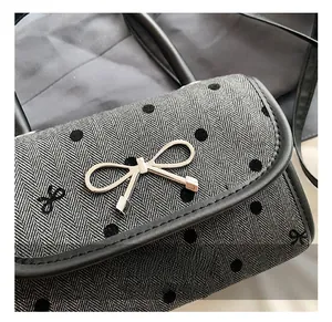 Close-up of golden bow-shaped metal clasp on gray herringbone fabric with embroidery