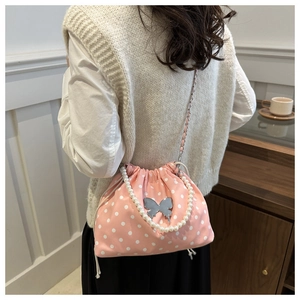 Detail view of pink polka dot drawstring bucket bag with pearl strap and silver butterfly