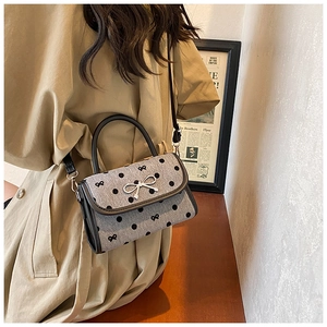 Detailed side view of polka dot crossbody bag with silver bow accent on a khaki coat