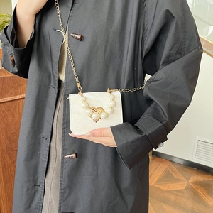 Cream white crossbody bag with pearl handle and gold heart clasp shown on a model