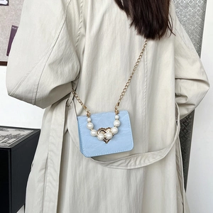 Light blue mini crossbody bag with pearl handle and heart lock shown on trench coat