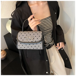 Detail of grey heart-print handbag with a silver metal bow and adjustable leather strap