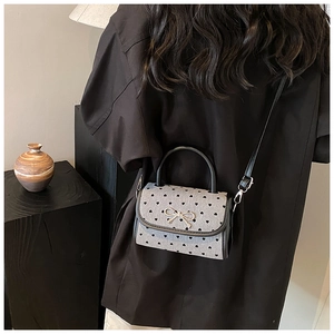 Detail of grey crossbody bag with black heart dots and silver bow worn by a model