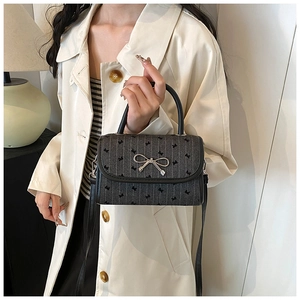Detail of grey denim crossbody bag with bow patterns and metallic bow lock buckle