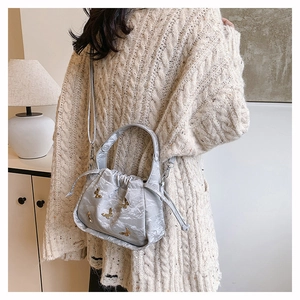 Detail of grey drawstring bucket bag with golden butterfly charms and textured finish