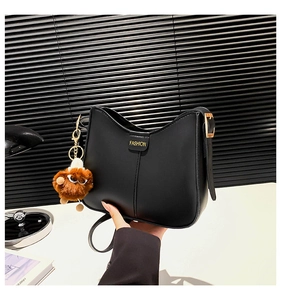 Detalle de bolso bandolera negro semicircular con hebilla dorada y amuleto de felpa