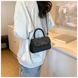 Polished black crossbody bag with bow buckle and dots shown on a model in a room