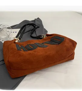 Detail of brown suede tote bag featuring black HOOD letter patch and gold metal ring