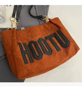 Detail of brown tote bag showing suede texture, letter patch and gold chain strap