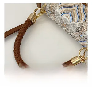 Detail of woven jacquard fabric bag with brown braided leather handle and gold hardware