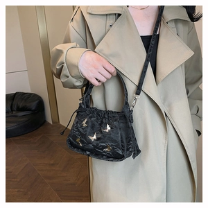 Detail of black pleated crossbody bag featuring a golden butterfly metallic buckle