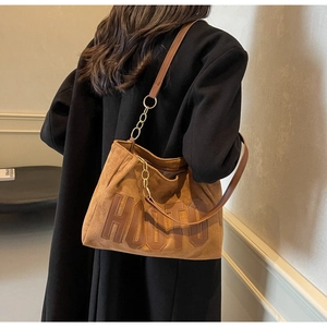 Detail of a large brown suede tote bag with HOUTO embossing and gold chain strap
