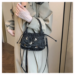 Detail of black drawstring bucket bag with pleats and gold butterfly metal accents