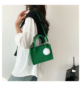 Detailansicht einer grünen gesteppten Filztasche mit weißem Pelzanhänger an einem Modell