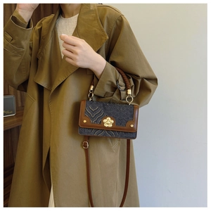 Detail of vintage square bag with jacquard pattern and floral metal buckle on a trench coat