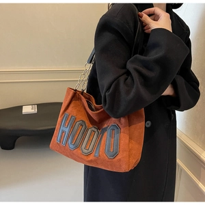 Detail of caramel suede tote bag with chain strap and bold HOOTO lettering on black coat